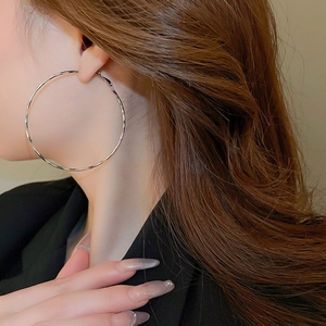 Macro detail of large silver hoop earrings worn by a model with long wavy hair