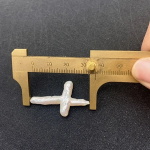 Caliper measuring a large baroque white freshwater pearl in a unique cross shape