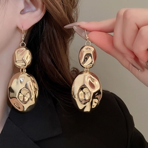 Close-up of model wearing large golden irregular oval earrings with glossy pleated finish