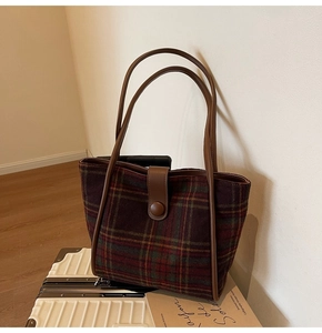 Detailed view of the plaid wool tote bag with brown leather handles on a suitcase