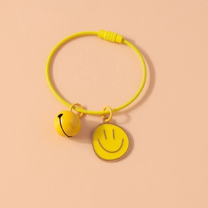 Macro shot of yellow wire bracelet featuring a small bell and a smiley face charm