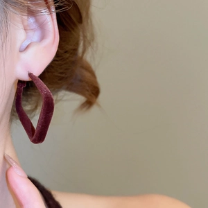 Gros plan de boucles d'oreilles géométriques en velours rouge foncé portées par un mannequin