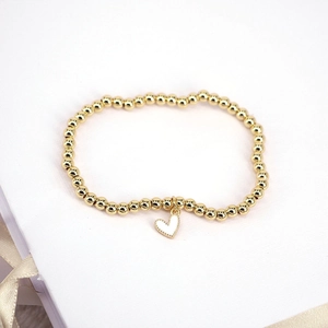 Golden beaded stretch bracelet featuring a delicate white heart charm on a book cover