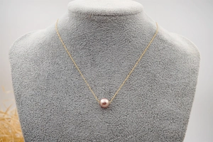 Detail view of pink pearl pendant on a thin gold chain worn on a grey neck model