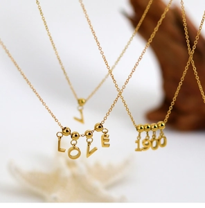 Close-up of golden necklaces with LOVE, 1900, and L letter pendants on fine chains