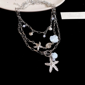 Detail of layered silver necklace with starfish shell charms and pearl on a plate