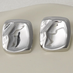 Detailed view of silver square stud earrings with irregular concave texture on a tray