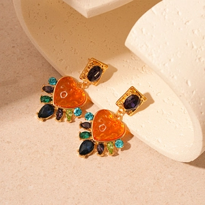 Detail of baroque earrings with purple gems and large orange resin heart charms