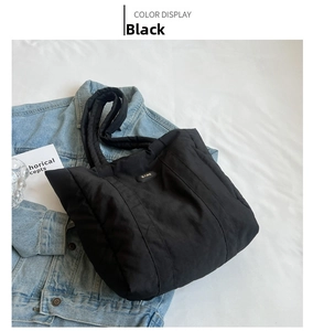 Detail of black quilted nylon tote bag with BARE logo on casual denim jacket