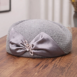 Detail of grey wool beret featuring a satin bow and silver rhinestone musical note brooch
