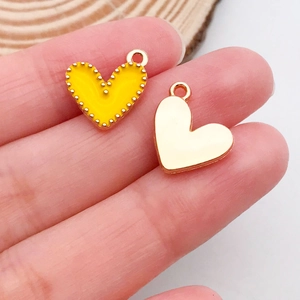Vue macro de mini breloques coeur en émail jaune et or pour bijoux DIY sur le bout des doigts