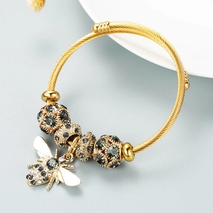 Detail view of golden spiral bracelet with rhinestone beads and a bee charm