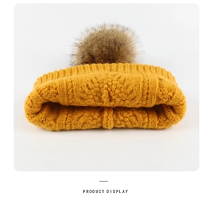 Detail of ginger yellow knitted winter hat featuring a fluffy brown faux fur pom pom