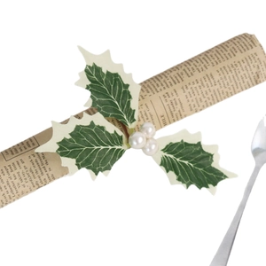Weihnachtlicher Serviettenring mit Stechpalmenblättern und weißen Perlen auf Zeitung