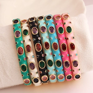 Row of colorful enamel bangles with vibrant gemstones on a soft white cushion display
