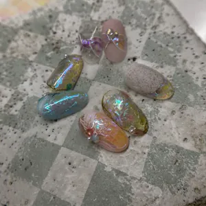 Dettaglio di adesivi per unghie aurora con accenti di perle e texture a conchiglia su pietra
