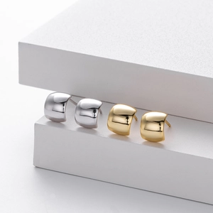 Primer plano de pendientes de arco en oro y plata sobre soportes blancos modernos