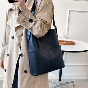 Minimalistische schwarze Leder-Tragetasche mit Fronttasche und verstellbarem Gurt am Trenchcoat