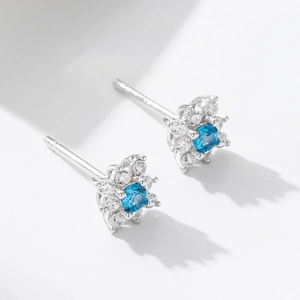 Macro shot of a flower-shaped silver stud earring with a central blue gem and white zircons