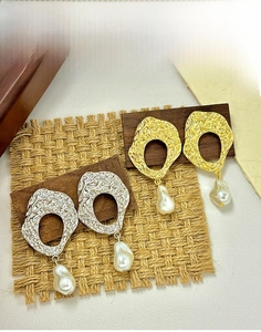 Detail of baroque pearl drop earrings featuring irregular wrinkled gold and silver metal textures