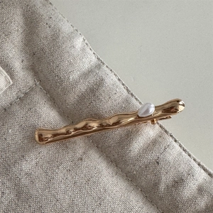 Close-up of golden wavy metal hairpin with a white pearl on a beige linen texture