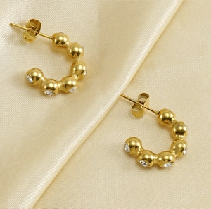 Detail of 18K gold-plated U-shape earrings with zircons on golden silk fabric