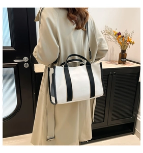 Minimalist white canvas tote bag with black straps worn over a classic beige trench coat