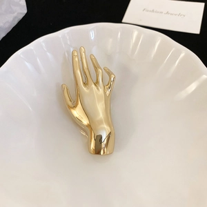 Macro shot of gold hand-shaped brooch with glossy mirror finish on a ceramic plate