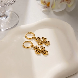 Vintage gold cross earrings with embossed patterns and crystals on white ceramic plate