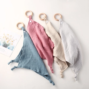 Close-up of four cotton gauze baby comforters with wooden teething rings in soft colors
