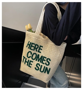 Detail of hand-woven beige tote with green 'HERE COMES THE SUN' text and interior capacity