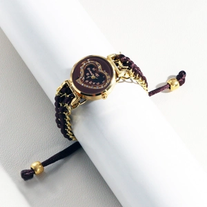 Detail of a gold watch with brown woven strap and crystal heart dial on a white display