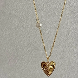 Detail of gold heart pendant with layered texture and a white pearl on the O-chain