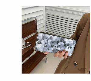 Close-up of long marble pattern wallet with gold zipper detail held by model