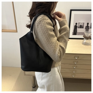 Close-up of minimalist black pebble grain leather bucket bag worn by a model in interior