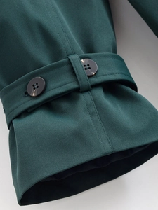 Detailed macro shot of dark green twill fabric and textured black button on the coat sleeve