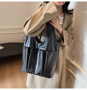 Detail of a large black leather shoulder bag with multiple functional pockets and a retro style