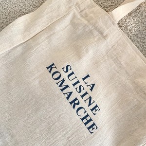Close-up of beige canvas tote bag showing textured fabric and blue lettering detail