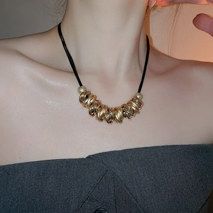 Detail of twisted gold metal pendant on a black leather cord necklace worn by a model