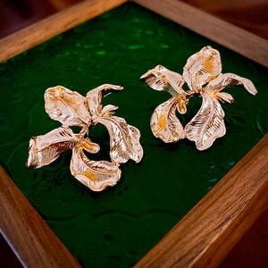 Detailed macro view of golden iris petal earrings on a vintage green embossed glass base