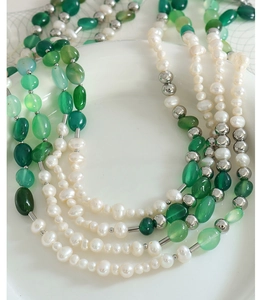 Dettaglio della collana di perle d'acqua dolce e agata verde su vassoio di ceramica bianca