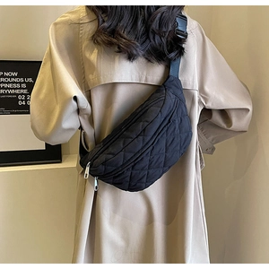 Detail of a black quilted crossbody bag with adjustable wide strap shown on a model