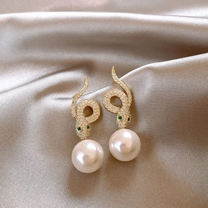 Close-up of gold snake earrings with sparkling diamonds and white pearls on silk