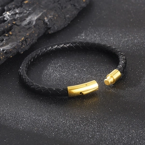 Men's black braided leather bracelet with golden magnetic clasp on dark stone surface
