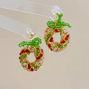 Detail of handmade beaded Christmas wreath earrings with red bows and gold hooks