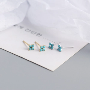Macro detail of silver and gold four-leaf flower earrings with turquoise beads