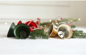 Nahaufnahme bunter Weihnachtsglocken aus Metall mit Schleifen auf verschneitem Boden