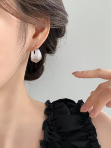 Close-up of silver C-shaped earrings with layered textured curves worn by a model
