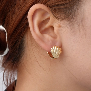 Close-up of a model wearing golden scallop shell textured hoop earrings in stainless steel