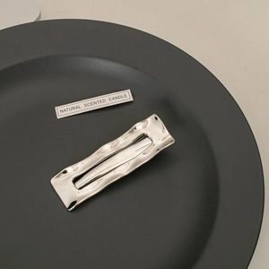 Macro detail of silver rectangular hair clip with wavy metal texture and hollow center